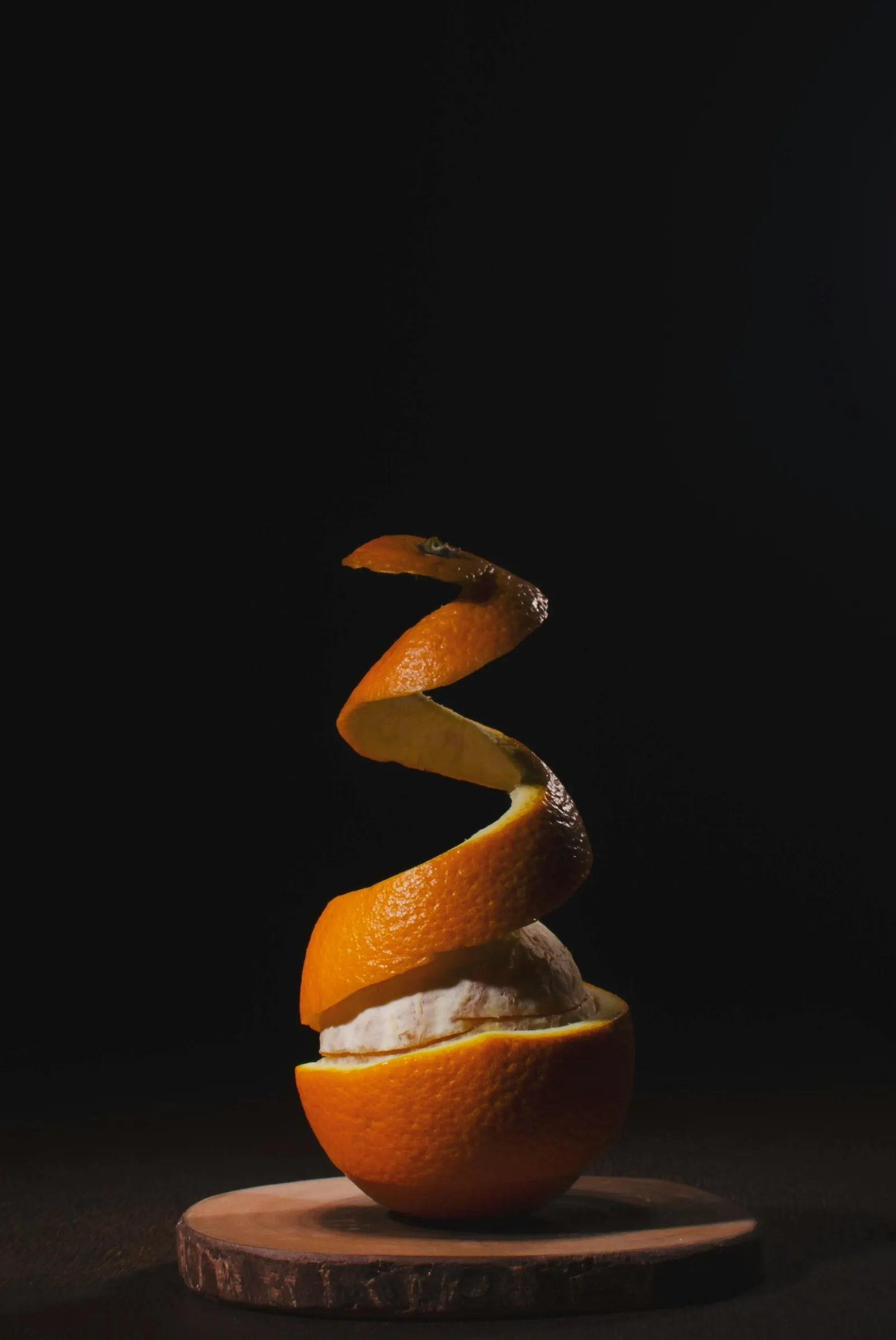 Orange partiellement épluchée, le zeste en spirale, posée sur un socle en bois.